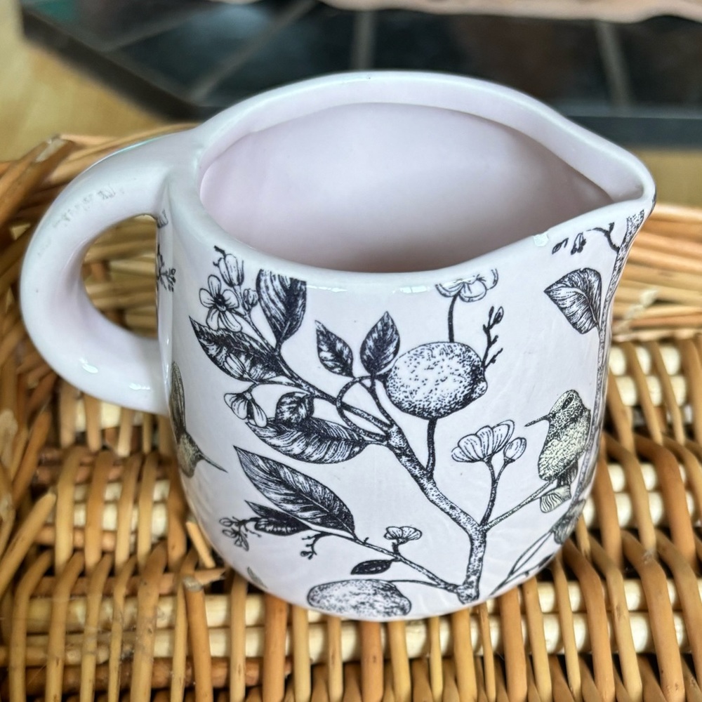 A pink ceramic creamer with a hummingbird and lemon tree design